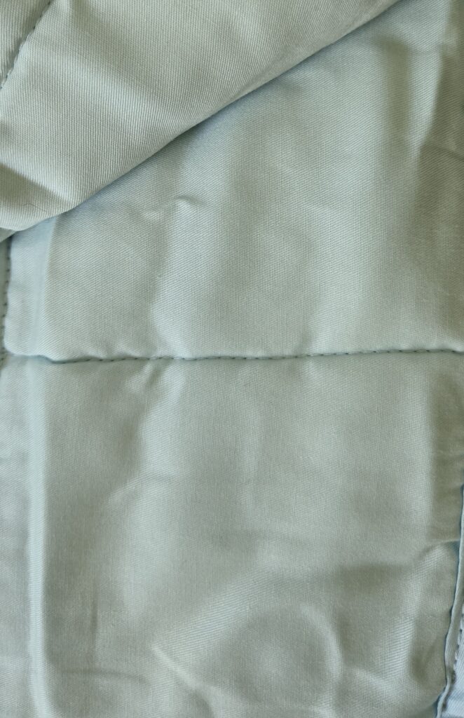 A light blue YnM weighted blanket spread out, showing the detailed grid stitching that creates small pockets for even weight distribution